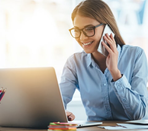 Businesses women talking on the phone happily while staring at laptop screen