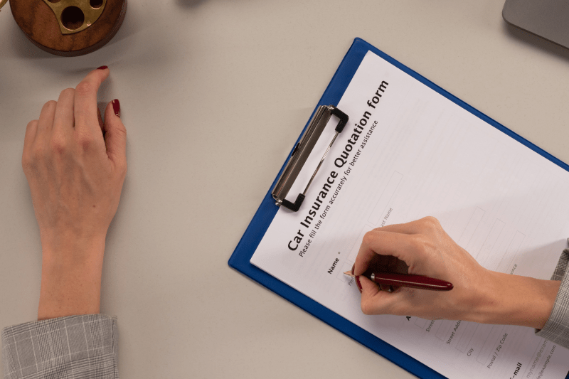 A young lady holding a pen and filling an auto insurance form